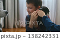 Smiling boy cuddling a puppy indoors with a dog watching nearby 138242331