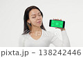 Adult young woman holds a phone with a green screen and smiles white background isolated space 138242446