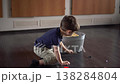 Young Boy Kneeling By Basket Placing Last Toys Inside, Satisfied Pause, Tidy Floor And Warm Room Light 138284804