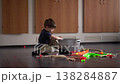 Young Boy Placing Toy Into Basket, Tidying Colorful Train Parts On Floor, Concentrated Gesture, Warm Cabinet 138284887