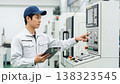 A worker inspects the control panel in a factory's NC-controlled manufacturing environment. A worker inspects the control panel in a factory's NC-controlled manufacturing environment. 138323545
