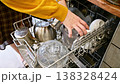 Woman loading dirty dishes into dishwasher, kitchen setting with utensils 138328424