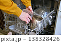 Woman places drty dishes into dishwasher rack, kitchen setting visible 138328426