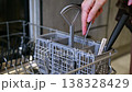 Kitchen utensil basket being filled with cutlery inside dishwasher 138328429
