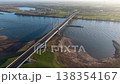 Aerial view of a cable stayed bridge over a wide river, with a large cargo vessel passing below, surrounded by green fields, rural houses, wind turbines, and calm countryside scenery. 138354167