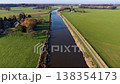 Aerial view of a rural landscape with a canal curving through green fields, two small road bridges crossing it, and a nearby house with outbuildings set among open farmland. 138354173