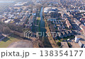 High angle aerial view of a narrow canal flowing through a modern European town with residential buildings, paved streets, and urban greenery under soft daylight. Drone shot. 138354177