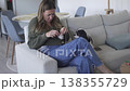 Woman crocheting at home while sitting on a sofa with her Cavalier King Charles Spaniel nearby. Cozy 138355729