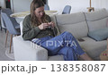 Woman crocheting while sitting on a sofa at home. Cozy lifestyle scene focused on handmade craft 138358087