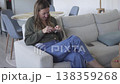 Young woman crocheting while sitting comfortably on a couch at home. Relaxed indoor scene focused on 138359268
