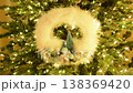 A Christmas wreath with feathers, fir trees, and small baubles against the backdrop of a bright garland. A perfect home decoration for Christmas and New Year. A cheerful mood. 138369420