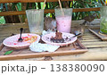 Three zebra doves eating leftover chocolate cake and crumbs from pink plates on a bamboo table at an outdoor cafe. Natural scavenger behavior in a tropical restaurant setting with cold drinks. 138380090