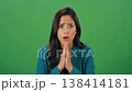 A young woman with dark hair reacts with shock and disbelief, her eyes wide and mouth open, against a green screen. 138414181