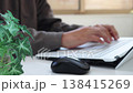 An image of a man working remotely in a brightly lit room (focus on the foreground, face not shown). 138415269