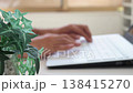 An image of a man working remotely in a brightly lit room (focus on the foreground, face not shown). 138415270