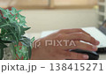 An image of a man working remotely in a brightly lit room (focus on the foreground, face not shown). 138415271