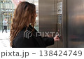 Side view of woman pressing elevator call button on modern stainless steel lift in shopping mall with soft indoor lighting. Urban lifestyle, accessibility and daily routine concept 138424749