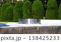 A stainless steel eternal flame burns on white stone in Hiroshima, Japan. Midday light casts crisp shadows as a lone visitor passes, evoking a solemn memorial mood. 138425233