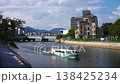 Midday view in Hiroshima, Japan, shows the Atomic Bomb Dome, a low arched bridge, a sightseeing boat on the Motoyasu River, pedestrians, offices, and parkland. 138425234