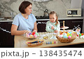 Mid shot of mother and daughter are preparing for the Easter holiday together. Little girl and a Caucasian woman decorate the room 138435474