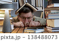 Tired man with book on head surrounded by stacks of books 138488073