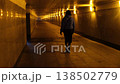 A person strolls alone through a narrow, illuminated tunnel at night in the city, creating an atmospheric and mysterious vibe while navigating the pathways. 138502779
