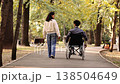Authentic representation of a young woman strolling alongside her male friend using a wheelchair, enjoying a leisurely walk in a serene park setting 138504649