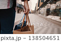 Customer walks along a sidewalk lined with storefronts, happily carrying shopping bags. The scene captures the essence of retail therapy in an urban commercial setting 138504651