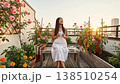 Tranquil rooftop garden setting with woman sipping tea among flourishing plants and city views 138510254