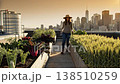 Woman looks after city garden. Sunset illuminates city skyline as woman tends crops on roof 138510259