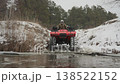 Red atv crossing icy stream, driver negotiates shallow ford, water splashes around treaded tires, snowbanks on banks, low front perspective, compacted ruts, muted winter light, calm steady pace 138522152