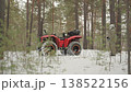 Red atv parked in snowy pine forest, stationary allterrain machine rests among slender trunks and frosty ground, wide knobby tires and heavy suspension visible, muted winter light creates calm outdoor 138522156