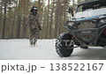 Camouflaged rider beside atv in snow, pine forest setting, rugged allterrain vehicle parked, rider inspects winch and front grille, full camo suit and helmet, snow packed tires, overcast light, quiet 138522167