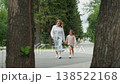 White mom and daughter paused talking, mother listening and offering comfort near tree trunk, calm summer afternoon on walkway, supportive embrace and soft gaze, casual clothing with hoodie and skirt, 138522168