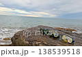 Three snorkeling masks rest on a rugged rock by the ocean. The waves gently lap against the shore as an overcast sky fills the background at dusk. 138539518