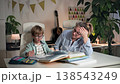 A mother and son are sitting at a table, she is explaining exercises to her son and helping him with his homework, both are really tired of it. They a sitting in bright room at a white table , where 138543249