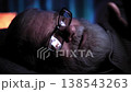 In dark room with low lighting elderly man in glasses lies in bed. He unable to sleep and watches news and commenting it on his smartphone. The screen of his smartphone is reflected in his glasses 138543263