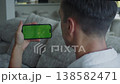 Green screen smartphone held horizontally by man sitting on sofa at home. Man holding mobile phone with chroma key display for screen replacement, apps, social media content or mobile interface mockup 138582471