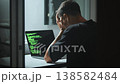 Hacker stressed at laptop during cyber attack, holding head while coding in dark room. Cybersecurity stress shows data breach risk, cyber attack pressure, digital threat and security failure situation 138582484