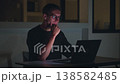 Man working late at night on laptop, typing code with focused expression and low light. Night work reflects overtime, dedication, productivity, deadlines and intense modern workflow 138582485