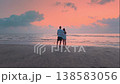Man and woman in love back view standing on the beach at sunset. Couple holds hands then embraces while looking at the sea together. Love relationship romance intimacy and emotional connection concept 138583056