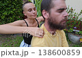 Woman Giving Shoulder Massage to Relaxed Bearded Man in Lush Outdoor Garden 138600859