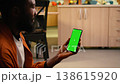 Vertical green screen mockup on phone next to African American man, sitting on the floor at home with cozy ambiance. Peaceful screen time in a comfortable warm indoor, modern lifestyle. 138615920