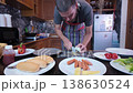 A bearded man is preparing hot dogs in the kitchen at home.  138630524