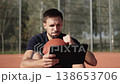 Caucasian man sits on basketball court with ball and tablet in hands and fiercely cheers for team game via online streaming. Portrait of fan with emotions of joy and elation. 138653706
