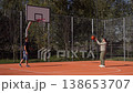 Caucasian man and woman playing basketball on outdoor court on sunny day. Pass and ball going into hoop with joyful emotions of couple leading active lifestyle. Cardio training and warmup. 138653707