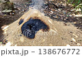 Wide Shot of Smoke curls from a charred mound of grain. Darkened seeds lie scattered atop the ash. Natural fire burns slowly in an outdoor setting. Earth, leaves, and debris surround the smoldering 138676772