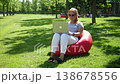 A young woman with a laptop sits in a red upholstered chair in a modern park. She closes her laptop and looks at the camera. A freelance woman in sunglasses is working in the park. Stable image. 138678556