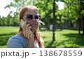 A picture of a contented lady wearing sunglasses, conversing on a sunny day in a verdant park. The image is unwavering. The camera remains steady. 138678559