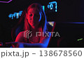 A gamer girl sits at a computer desk and puts on headphones with a microphone. She starts playing an online video game on her computer. A teenager in a computer club with neon lights puts on a headset 138678560